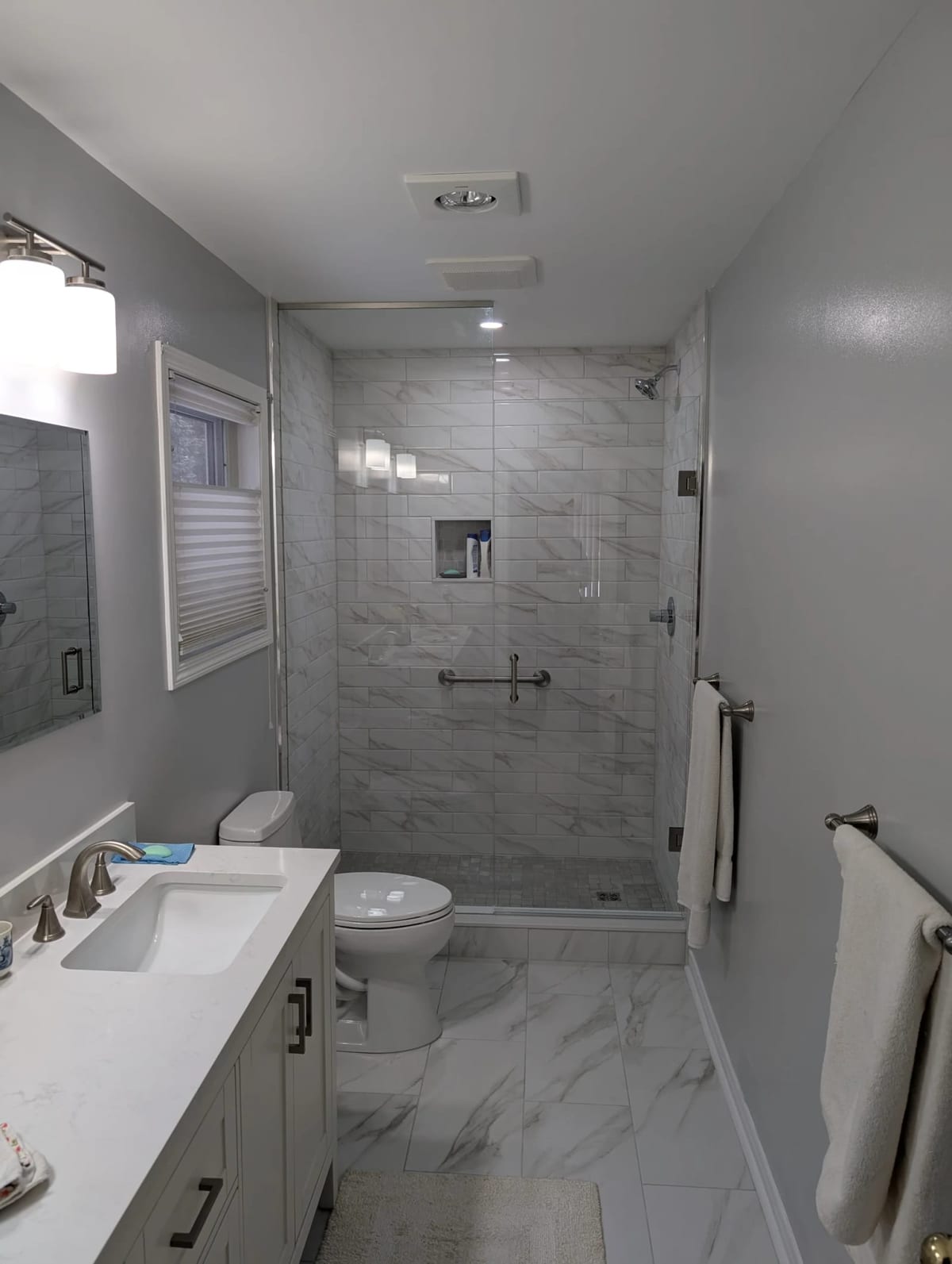 After: finished bathroom with a custom-tiled walk-in shower, glass enclosure, marble-look tile floor and new vanity at 23 Indiana Ave in Wasaga Beach