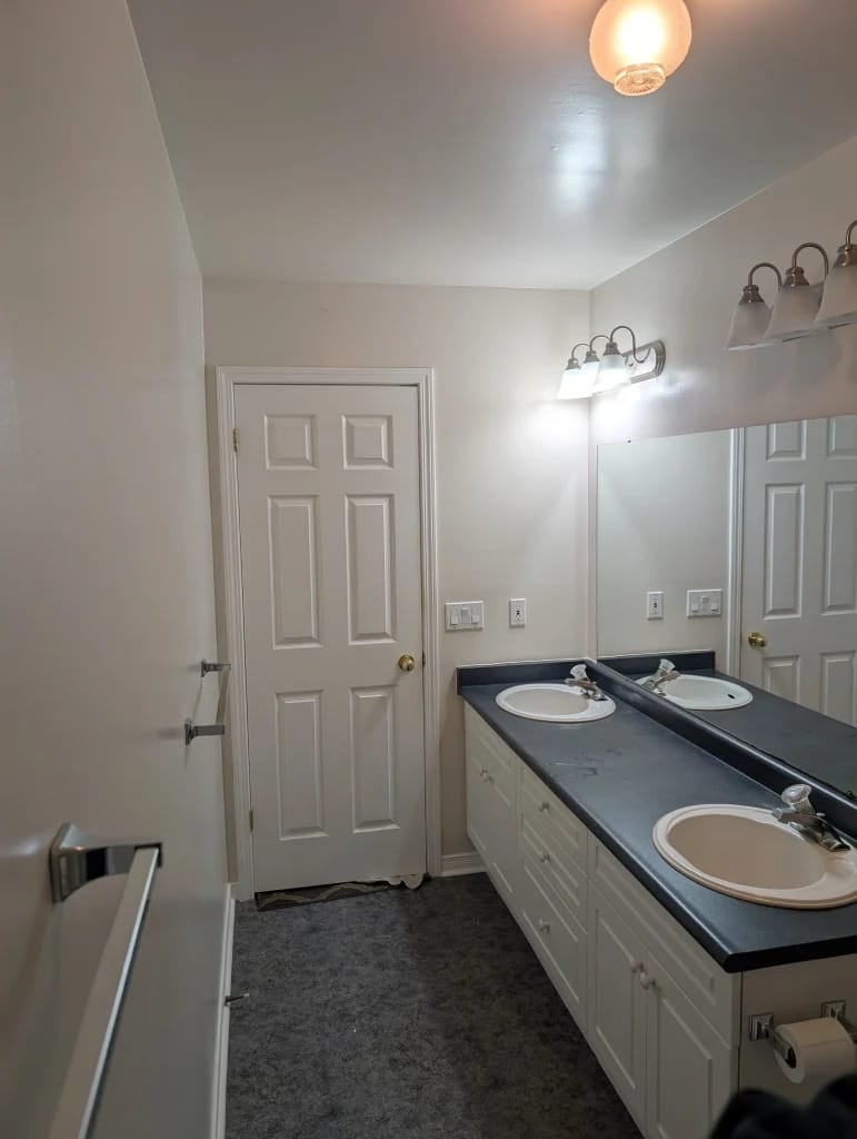 Bathroom before renovation at 23 Indiana Ave in Wasaga Beach, with a dated double vanity, laminate top and carpet-style flooring
